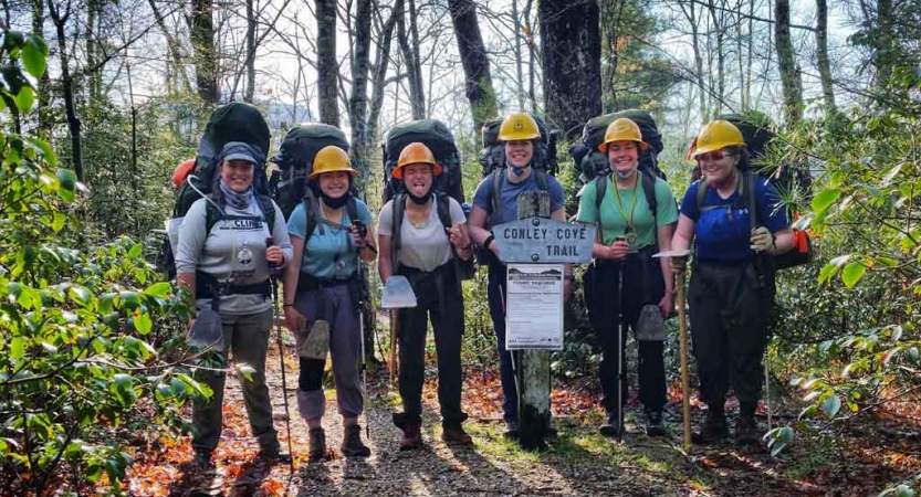 A group of people wearing helmets stand beside a trail sign